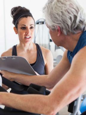 a fitness trainer works with a middle-aged man on an exercise bike