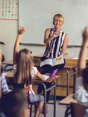 a teacher gets ready to call on a class of children with raised hands